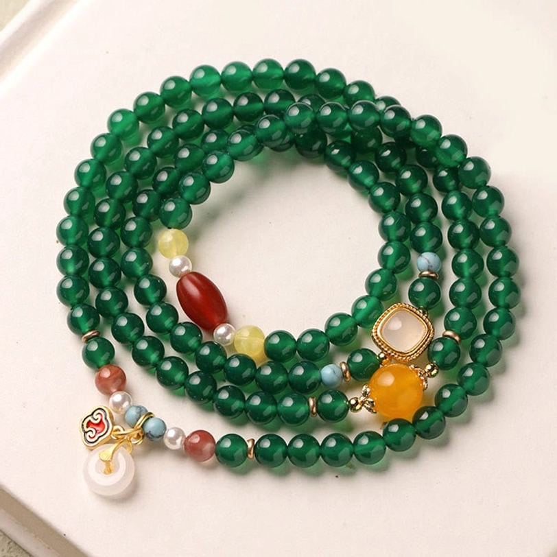 Close-up overhead view of coiled green agate Tibetan mala showing bead texture and decorative charms