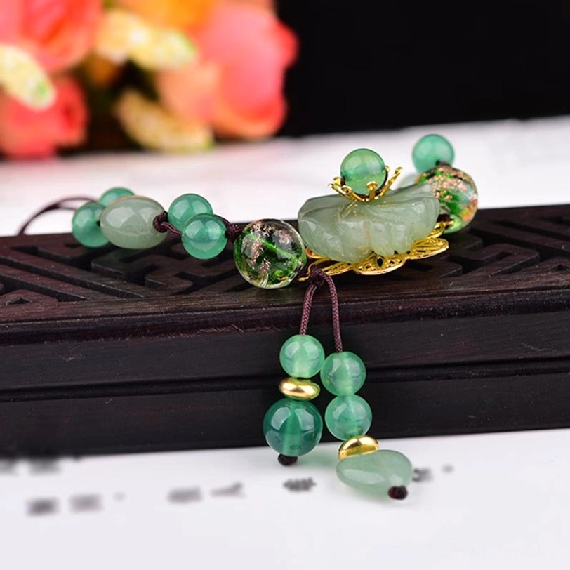 Close-up of flat carved green jade stone charm with gold metal accents on dark wooden background