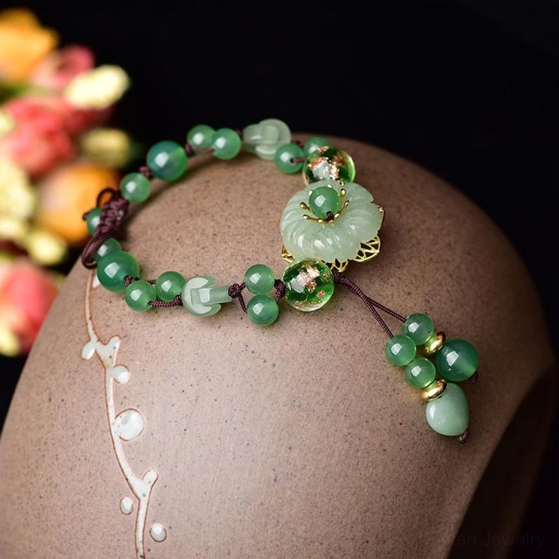 Detailed view of green jade flower charm with gold-toned metal accents displayed on ceramic jewelry stand