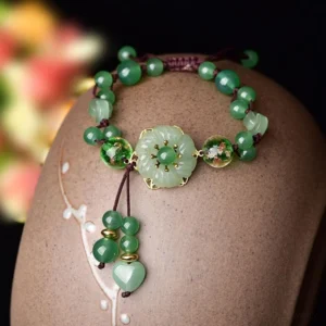 Close-up side view of green jade bracelet with glossy aventurine beads and dangling heart jade pendants on ceramic holder