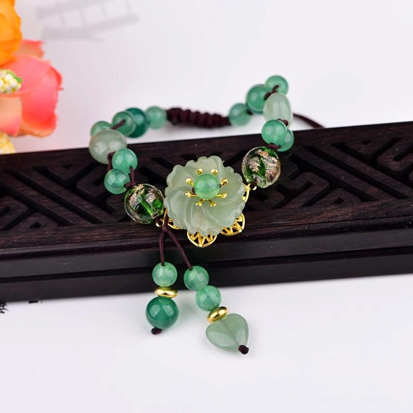Green jade flower bracelet with carved jade charm in gold metal frame displayed on dark wooden stand