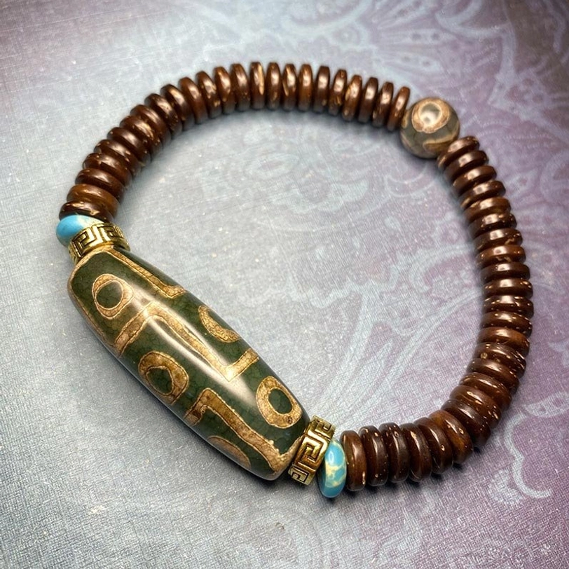 Green nine-eye dzi bead bracelet with turquoise metal spacers and brown agate beads on light gray textured background