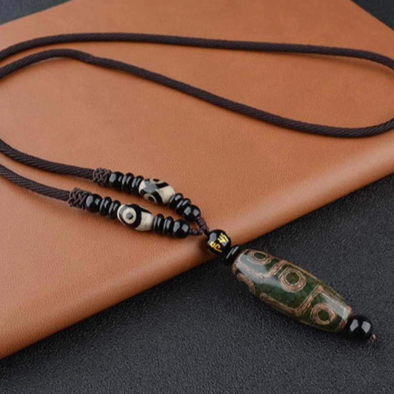Green Dzi bead necklace with polished agate pendant and adjustable woven cord on brown leather background, Tibetan spiritual wellness jewelry