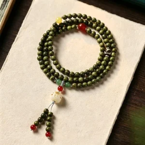 Green sandalwood cat charm mala bracelet with red accent beads, overhead shot on rice paper and wooden desk, showing multi-wrap design