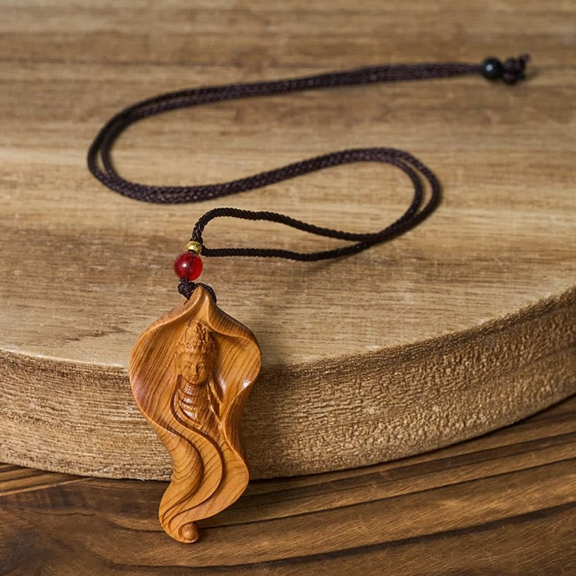 Guanyin wood pendant displayed on wooden coaster - side angle showing natural wood grain and braided rope attachment