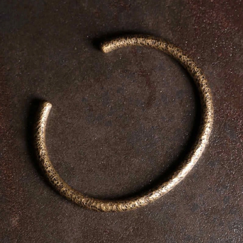 Single open-ended hammered copper cuff with textured surface, angled flat lay view