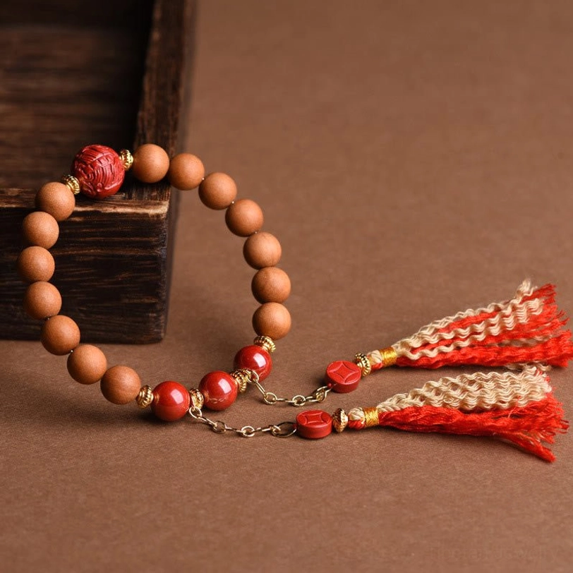 Hand-strung peach wood pixiu bracelet with carved red cinnabar and mixed red-beige dual tassels on craft paper flat lay