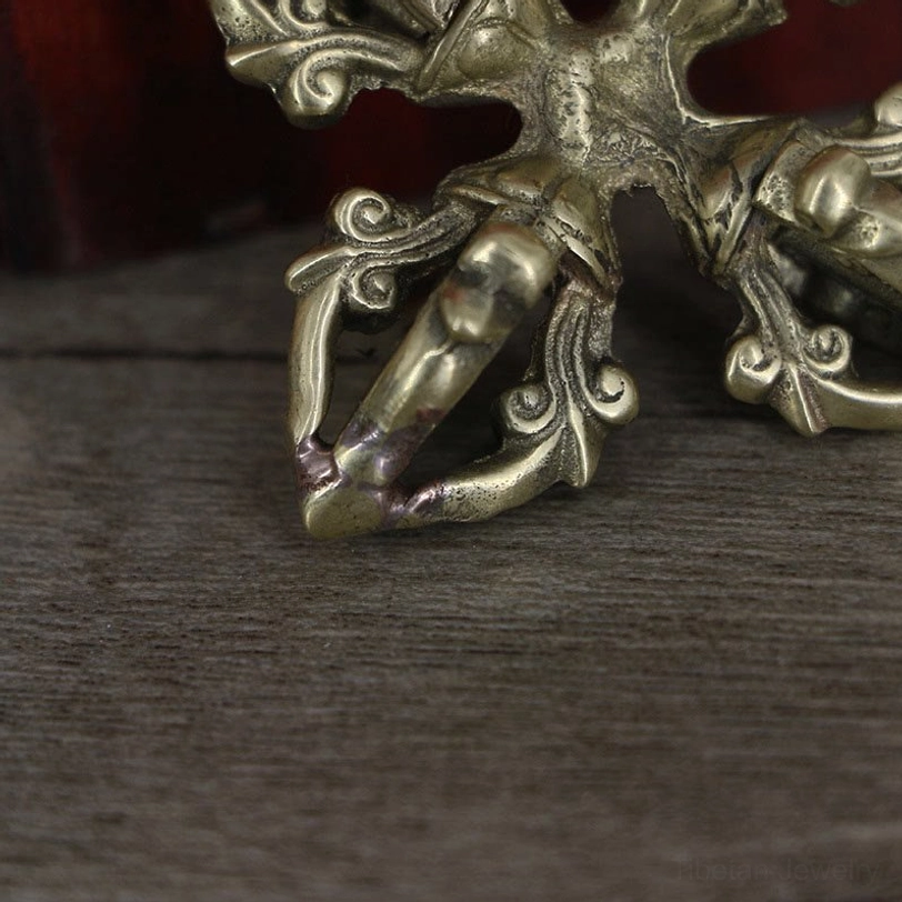 Extreme close-up of handmade copper dorje showing polished brass surface, worn metal tips on prongs, and intricate scroll decorations