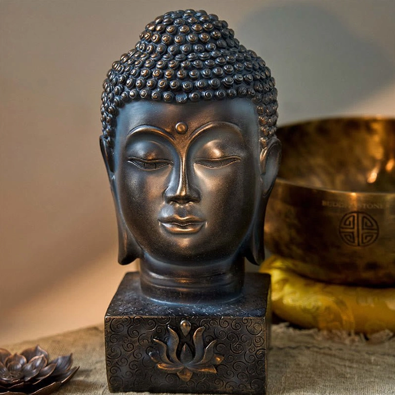 Buddha head statue with smooth aged metal finish and square lotus embossed base, displayed in meditation setting with singing bowl