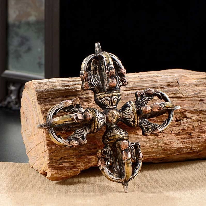 Symmetrical double dorje vajra displayed on wood block featuring detailed Buddhist motifs and aged metal patina