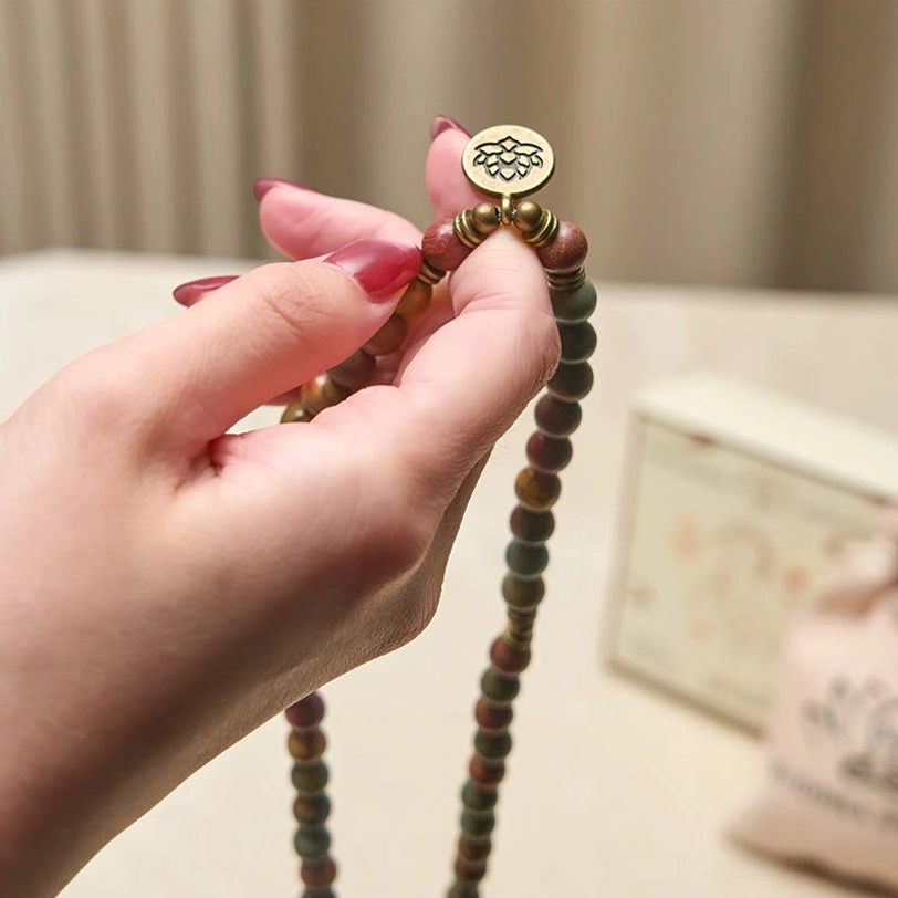 Handmade lotus charm mala held in hands close-up showing individual red turquoise beads and brass pendant