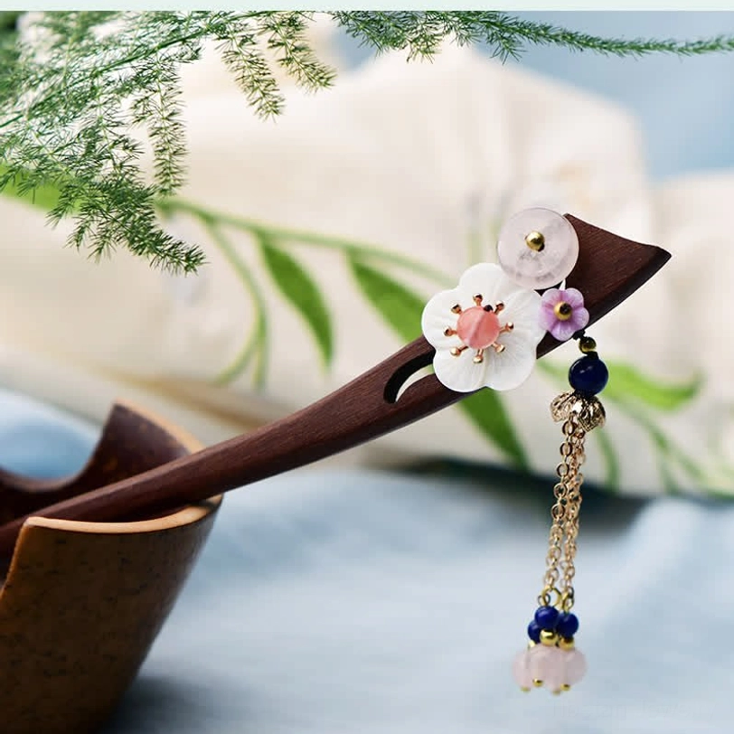 Wooden healing hairpin with pink flower center and dangling chain tassel on natural fabric