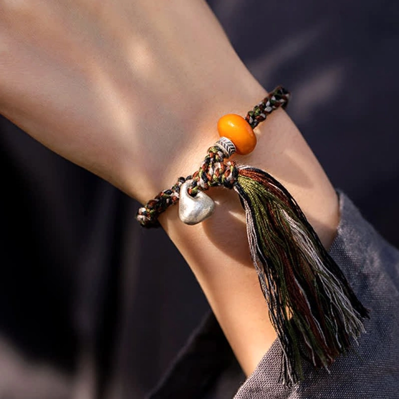 Detailed close-up of handmade Tibetan protection bracelet on wrist featuring amber centerpiece, sterling silver charm, and woven cord