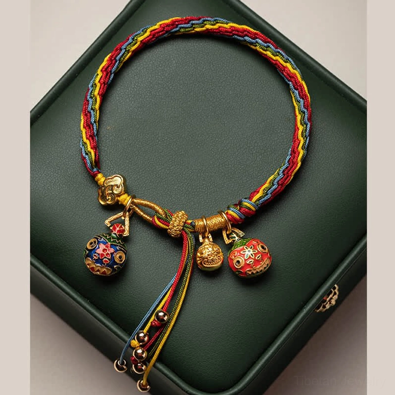 Handmade Tibetan bracelet in storage box with multicolor woven rope, gold hardware, and three enamel pendants