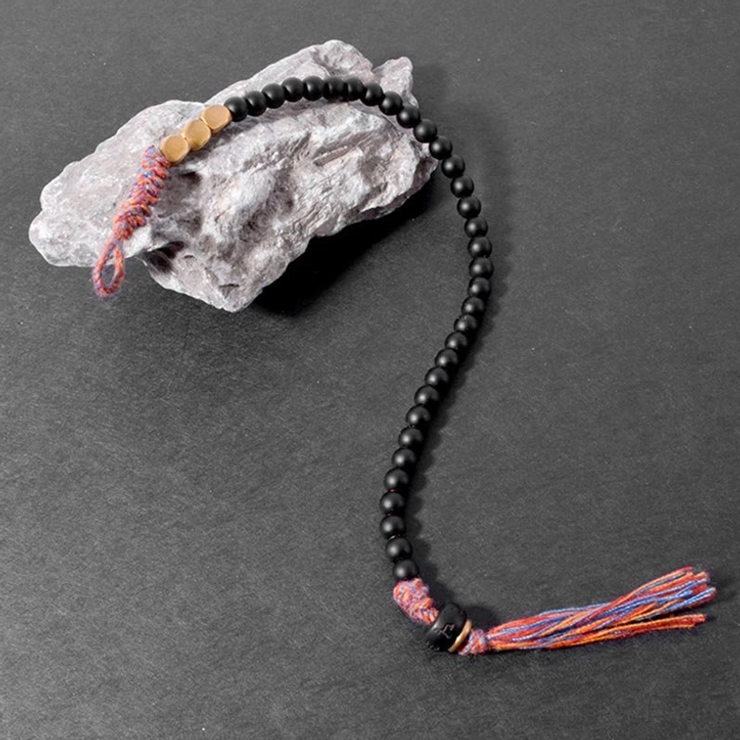Fully stretched Tibetan black onyx bracelet featuring colorful woven tassel and gold metal decorations against stone texture