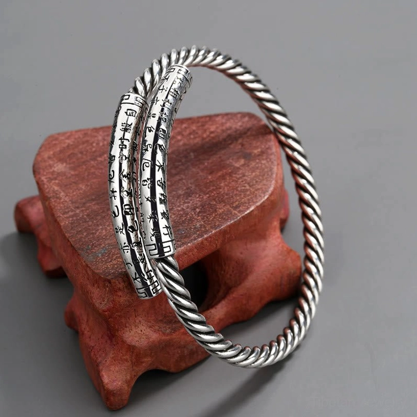 Antique silver-tone Heart Sutra copper bangles - three-quarter oblique view on red wooden stand showing twisted band and engraved sutra