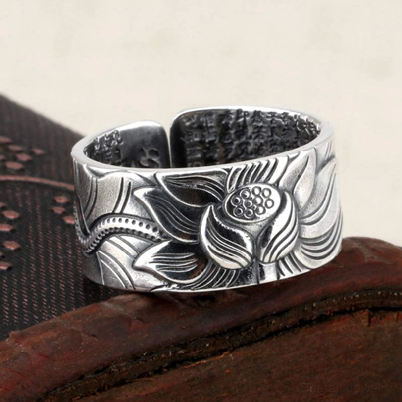 Sterling silver lotus and heart sutra protection ring showing raised lotus relief carving with full sutra text engraved inside, top view on dark carved wooden base