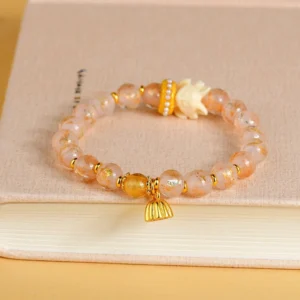 Tibetan incense ash liuli glass beads bracelet flat lay showing nine-tailed fox charm and gold lotus pendant on notebook