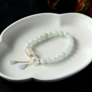Pale green jade beaded bracelet with delicate shell flower and dual teardrop pendants on white ceramic tray