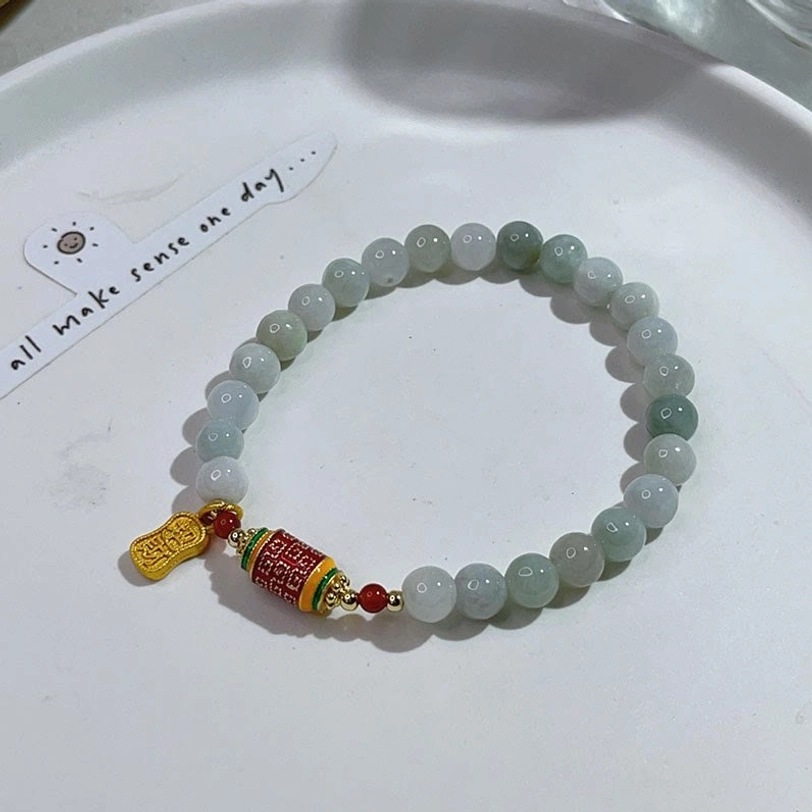 Jade fu prayer wheel bracelet flat lay on ceramic plate showing ombre green beads and decorative charms