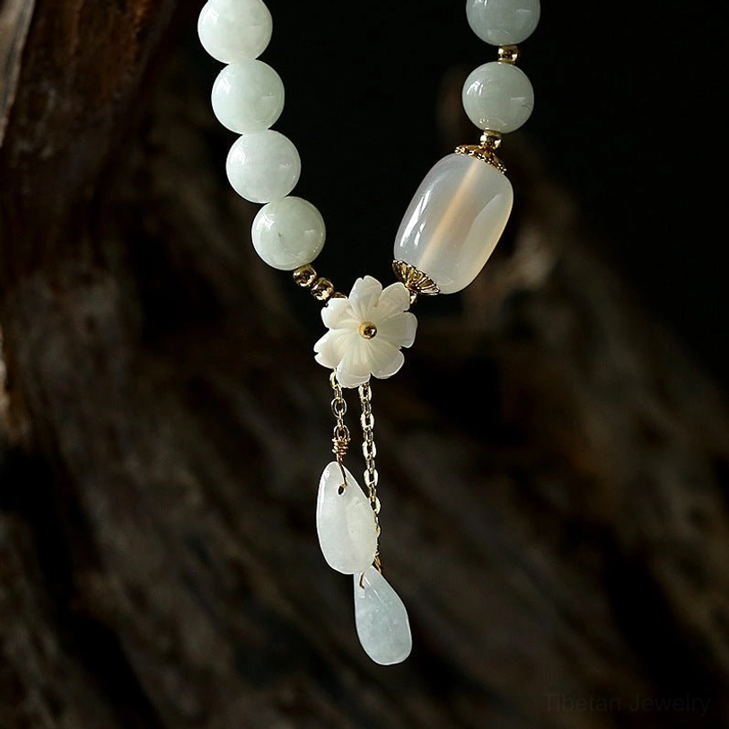Jade pendant necklace with round jade beads, shell flower, and long teardrop pendants hanging on dark wood