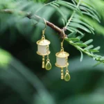 925 sterling silver jade prayer wheel drop earrings with green teardrop jade stone pendant, outdoor natural lighting on conifer branch