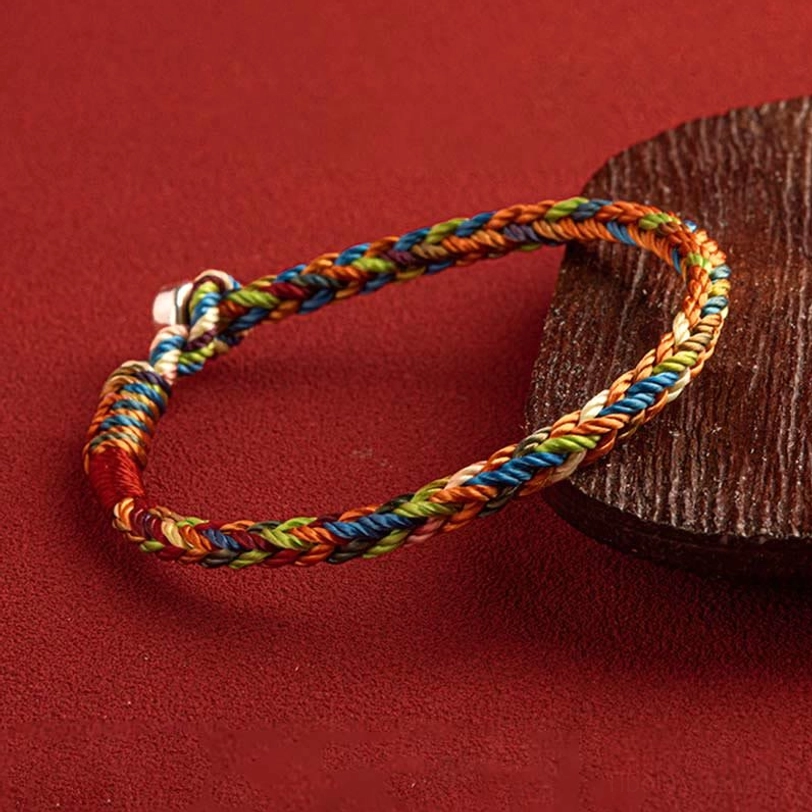 Handcrafted multicolored braided protection bracelet side angle view with silver toggle fastener on wooden coaster
