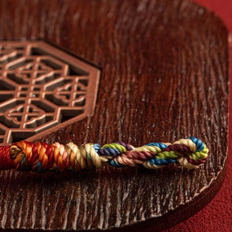 Handcrafted multicolored braided bracelet segment on carved wooden coaster highlighting thick knot weave and wood grain