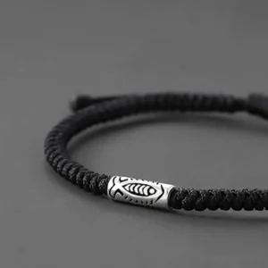 Close-up side view of black braided cord koi fish bracelet with twisted rope texture and silver charm