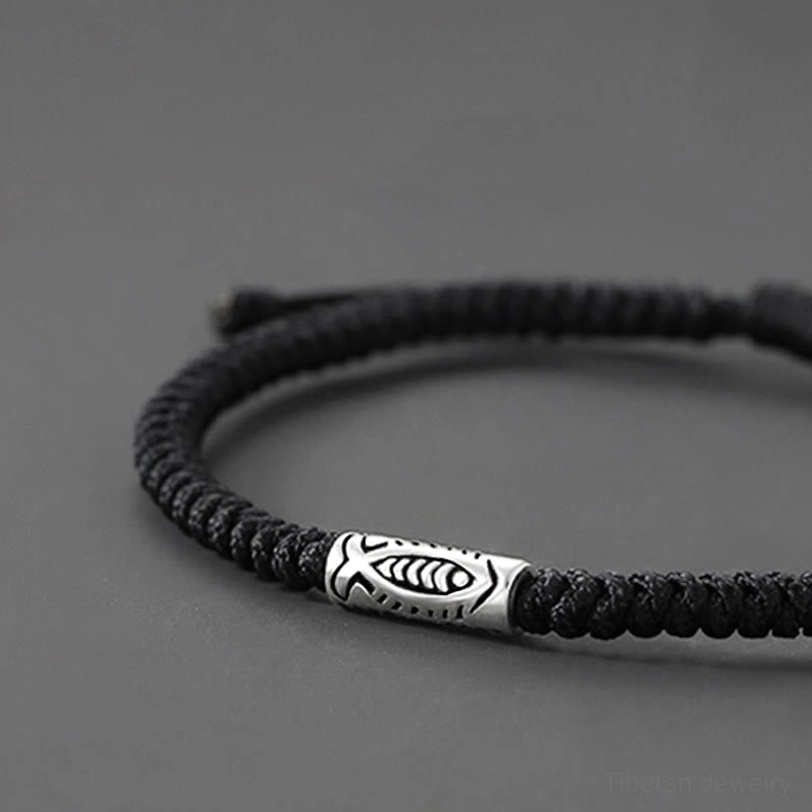 Close-up side view of black braided cord koi fish bracelet with twisted rope texture and silver charm