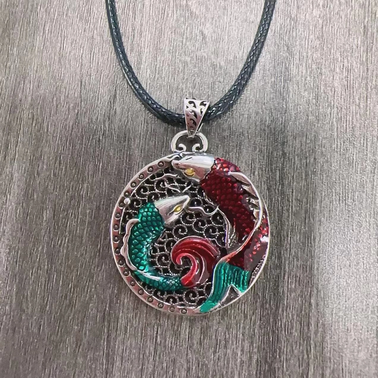 Koi fish pendant necklace with black leather cord, flat lay showing detailed enamel koi decoration on grey wood grain background