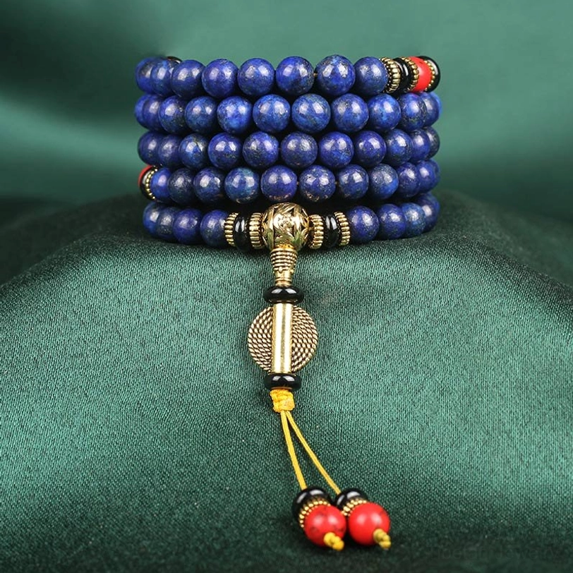 Stacked lapis lazuli 8mm mala beads on dark velvet showing coiled blue stone with bronze hardware and red charm tassel