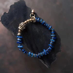 Deep blue lapis lazuli beads with carved metal accent and bronze hardware, top-down view on stone background