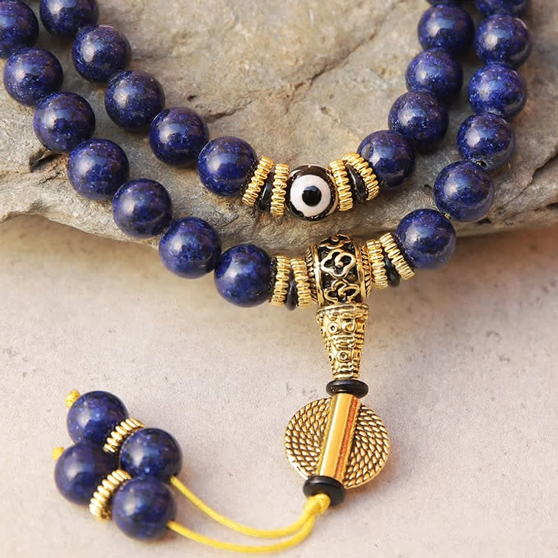 Close-up of lapis lazuli mala beads showing evil eye dzi bead, ornate gold metal fittings, and natural stone texture with pyrite flecks