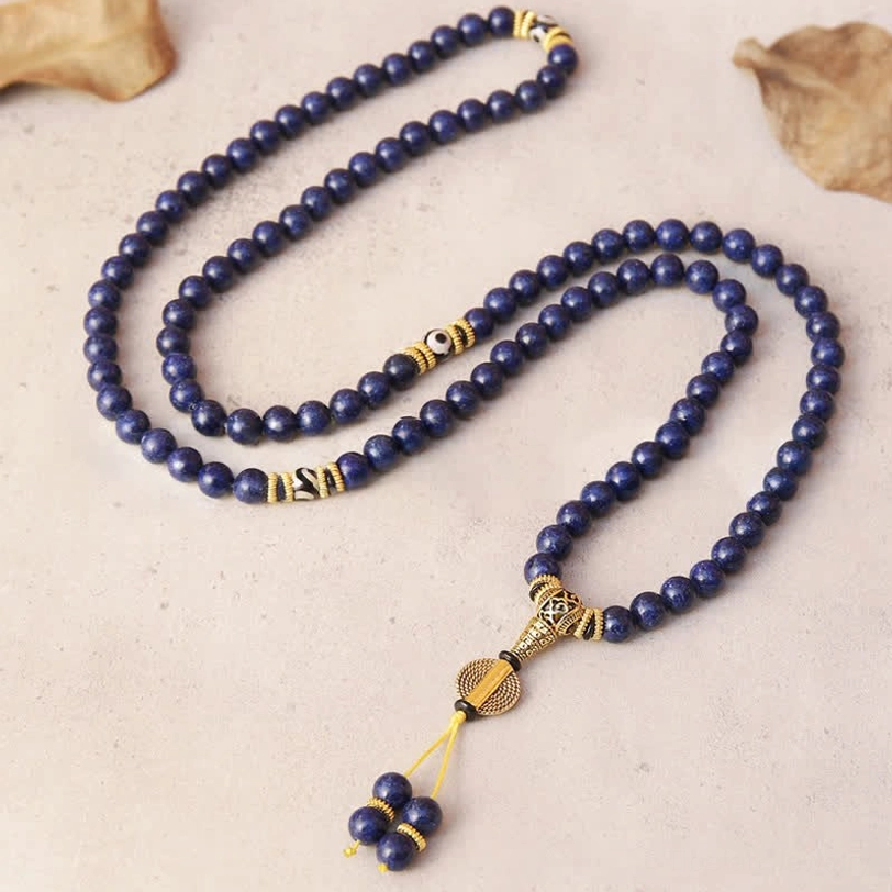 Flat lay coiled lapis lazuli mala necklace with gold metal hardware and beaded tassel on light background