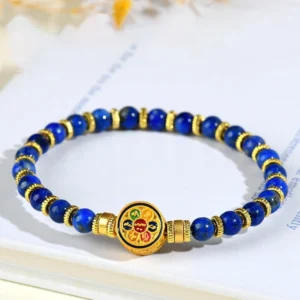 Lapis lazuli Om Mani Padme Hum bracelet with gold metal spacers and enamel mantra charm displayed on white book background