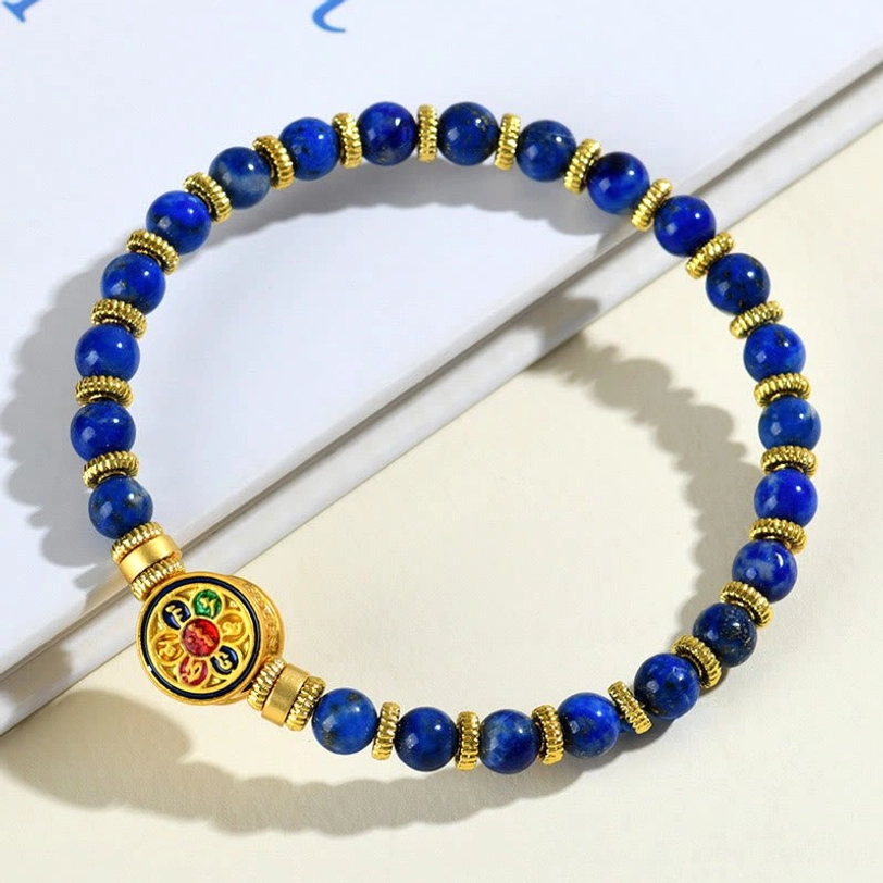 Blue lapis lazuli beaded bracelet with gold accents and sacred mantra medallion on light gray background