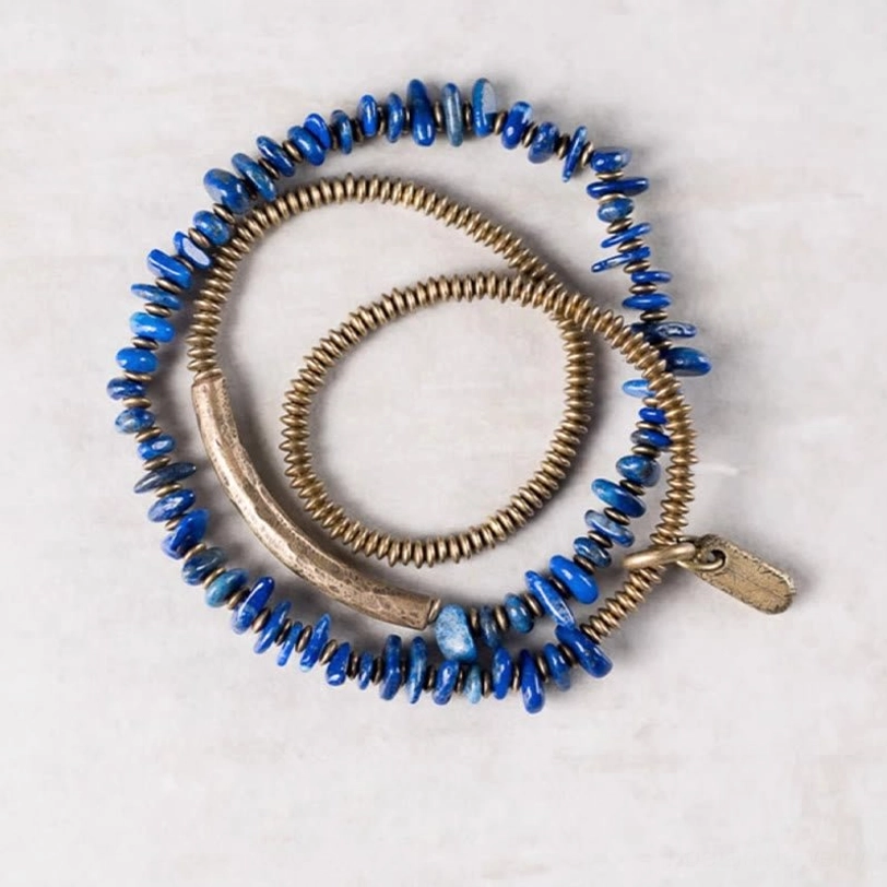 Flat lay view of lapis lazuli triple wrap bracelet with brass curved tube and metal tag on white background