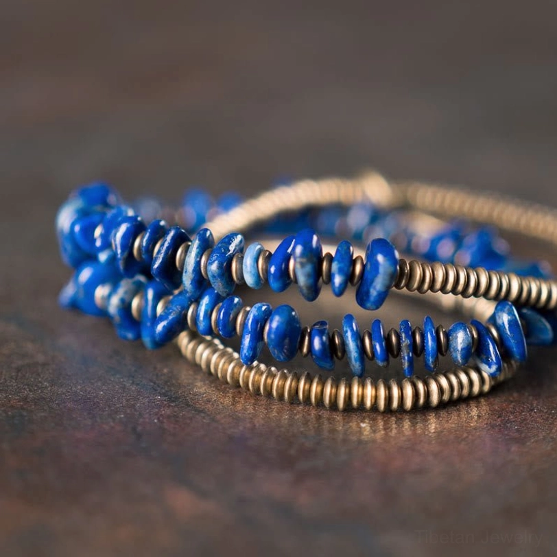 Close-up overhead view of stacked lapis lazuli triple bracelet strands with blue chips and brass beads on dark background