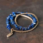 Lapis Lazuli triple wrap bracelet with copper beads and brass tube, top-down side angle view on dark matte desktop