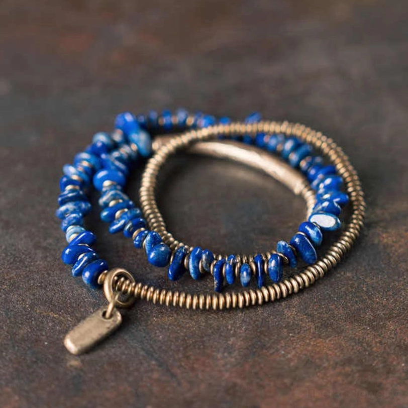Lapis Lazuli triple wrap bracelet with copper beads and brass tube, top-down side angle view on dark matte desktop
