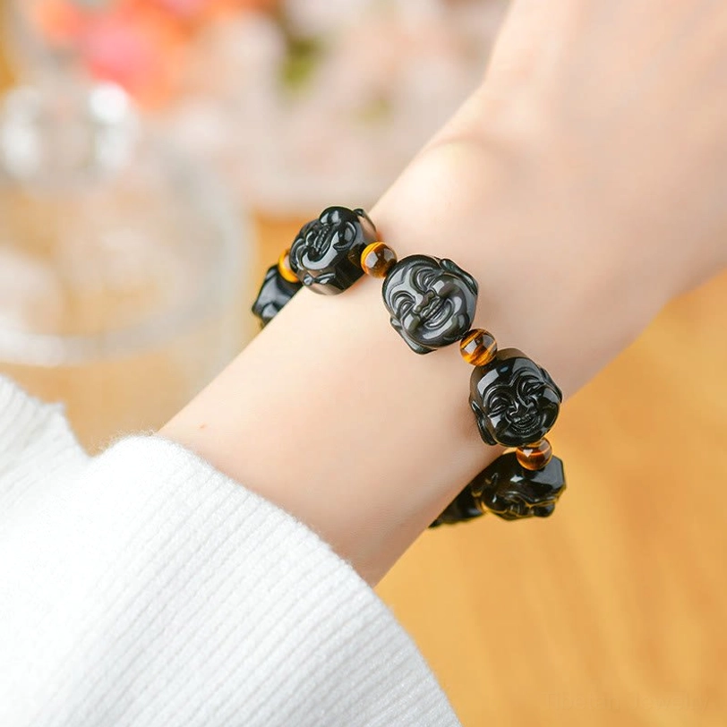 Laughing Buddha obsidian bracelet side wrist view - detailed carved Buddha beads with amber spacer details on cozy background