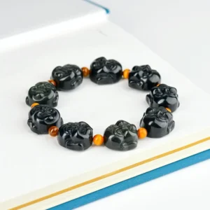 Laughing Buddha obsidian bracelet flat lay on notebook - full strand with carved Buddha heads and orange spacer beads