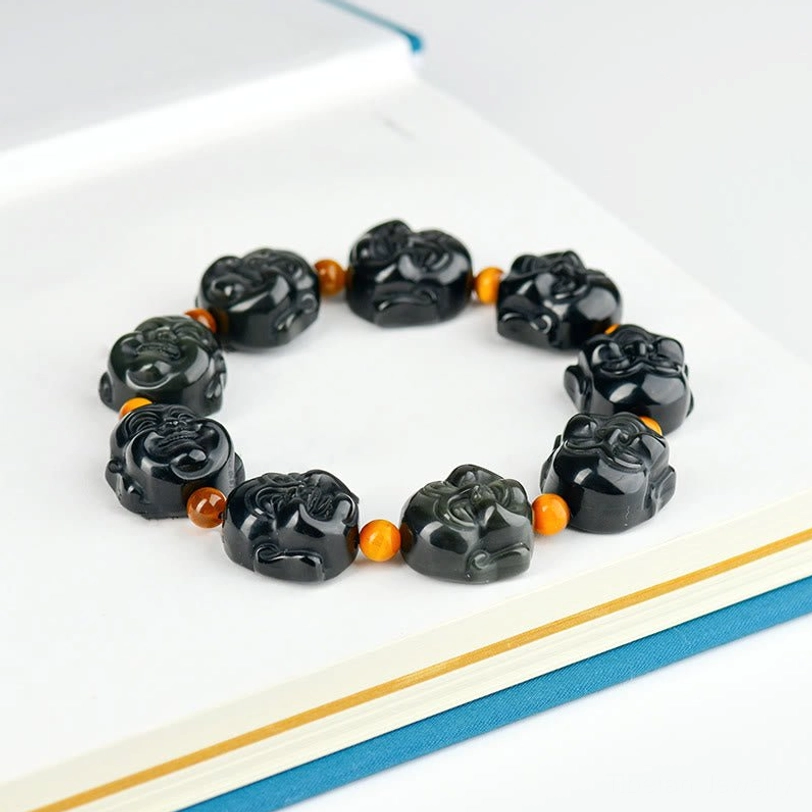Laughing Buddha obsidian bracelet flat lay on notebook - full strand with carved Buddha heads and orange spacer beads
