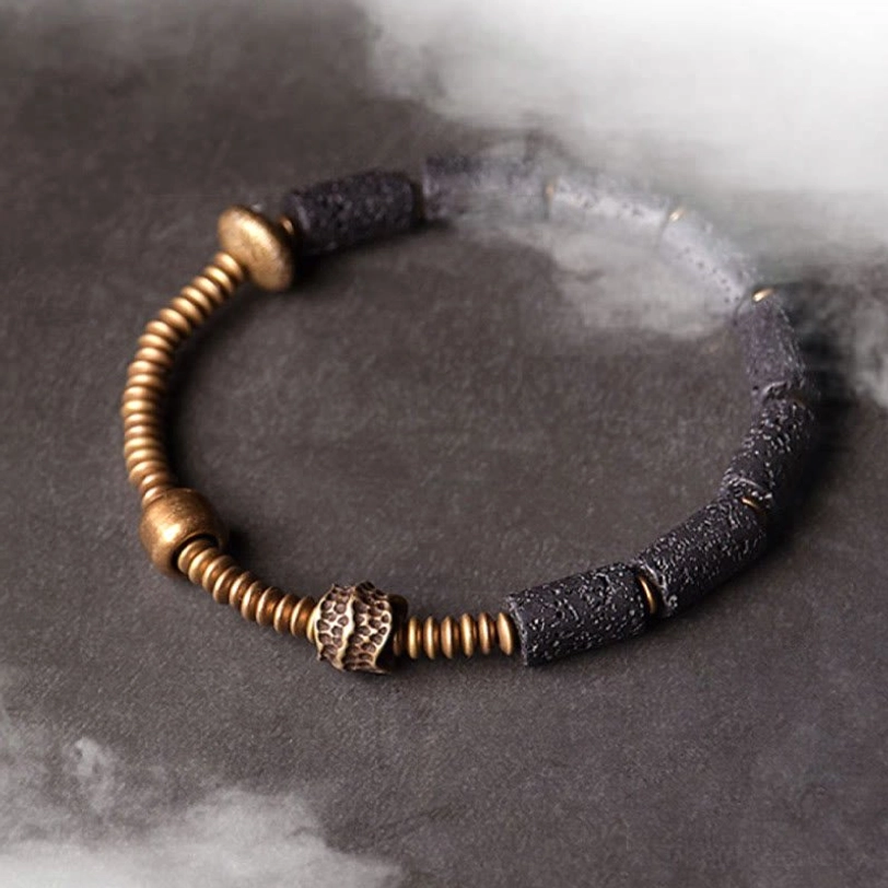 Atmospheric moody flat lay of lava rock copper bracelet on dark smoky background highlighting natural stone appearance