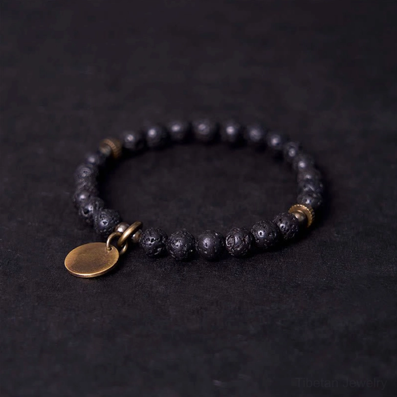 Three-quarter side angle of black lava rock bracelet showing copper charm detail and textured bead surface