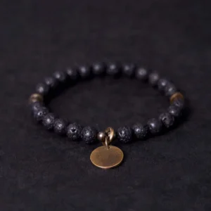 Lava rock healing bracelet with copper charm displayed flat, showing black porous beads and bronze round pendant on dark background