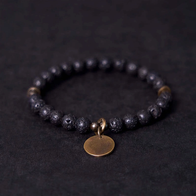 Lava rock healing bracelet with copper charm displayed flat, showing black porous beads and bronze round pendant on dark background