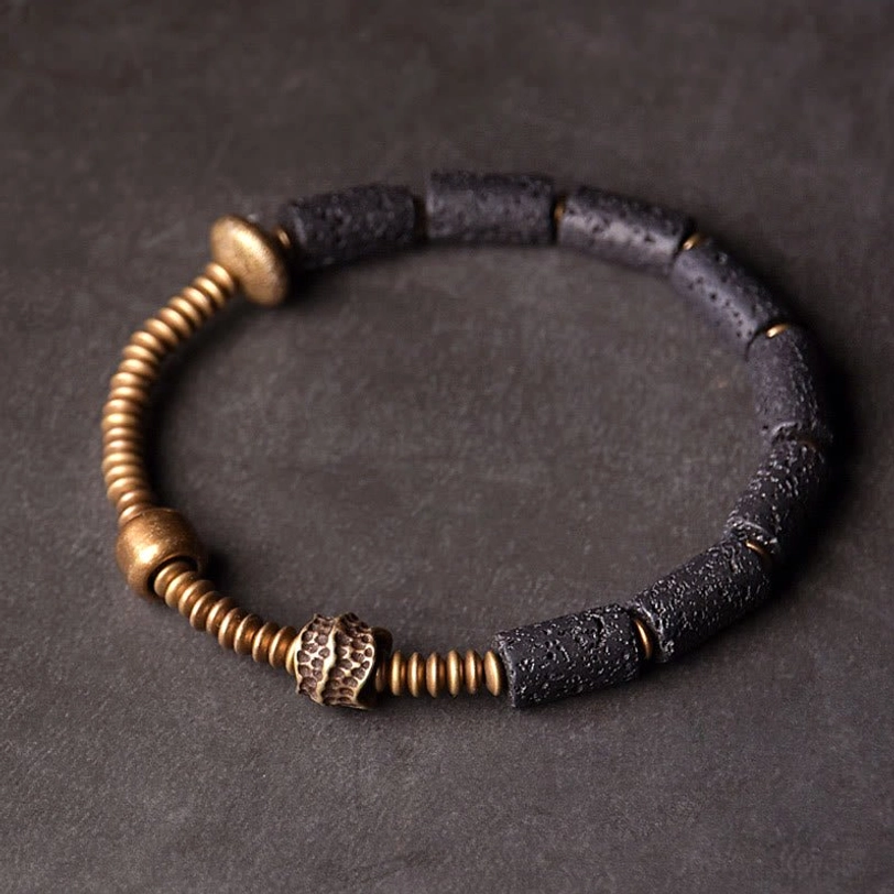 Lava rock copper wealth bracelet flat lay top view with black cylindrical beads and antique copper accents on dark background