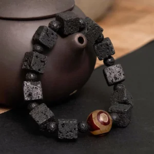 Close-up side view of Lava Rock Dzi Bead Bracelet showing textured matte black lava blocks, tiny round spacer beads, and hand-painted three-eye Dzi bead focal point